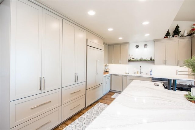 kitchen with light stone counters, sink, paneled built in refrigerator, and light hardwood / wood-style floors