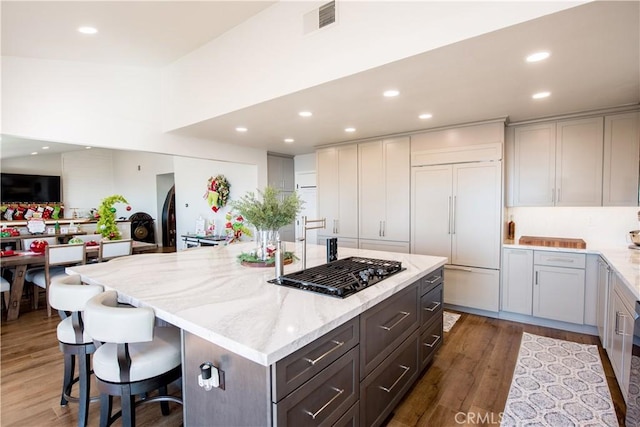 kitchen featuring a breakfast bar, a center island, dark hardwood / wood-style floors, paneled fridge, and light stone counters