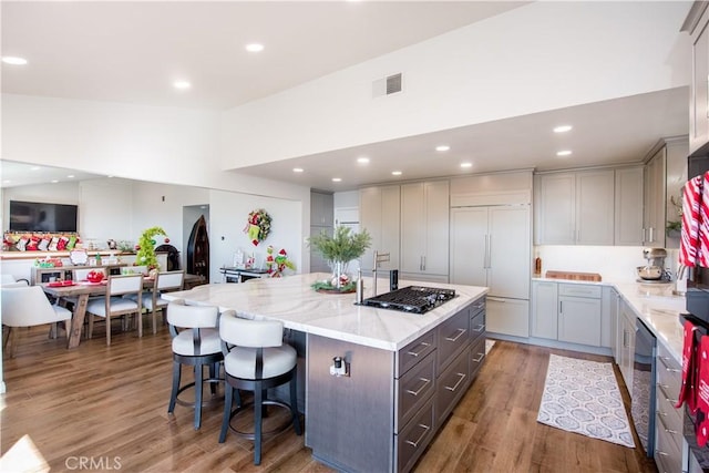 kitchen with light stone countertops, a kitchen breakfast bar, paneled built in refrigerator, wood-type flooring, and a center island