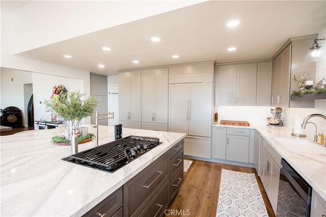 kitchen with sink, dishwasher, stainless steel gas cooktop, light hardwood / wood-style flooring, and paneled built in fridge