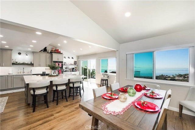 dining area featuring light wood-type flooring, sink, and high vaulted ceiling