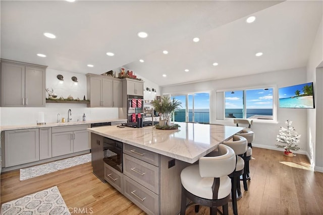 kitchen featuring built in microwave, light stone counters, light hardwood / wood-style floors, lofted ceiling, and a kitchen island