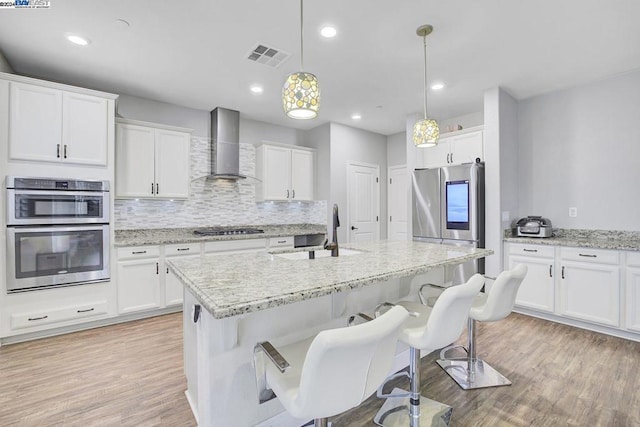 kitchen with pendant lighting, appliances with stainless steel finishes, wall chimney exhaust hood, white cabinetry, and sink