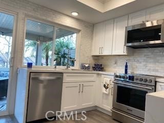 kitchen with white cabinets, light wood-type flooring, appliances with stainless steel finishes, and decorative backsplash