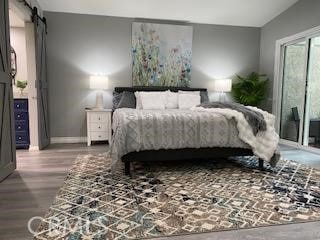 bedroom with wood-type flooring, a barn door, and vaulted ceiling