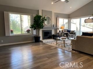 living room featuring vaulted ceiling, ceiling fan, hardwood / wood-style flooring, and a brick fireplace