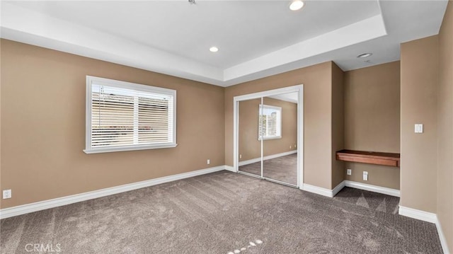 unfurnished bedroom with a tray ceiling, a closet, and dark carpet