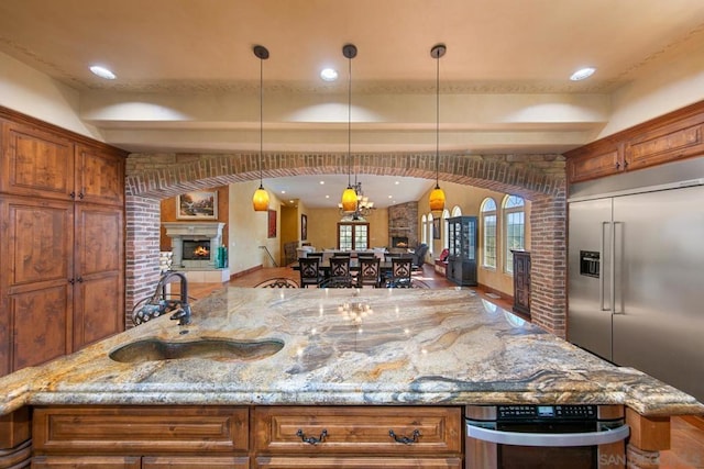 kitchen with pendant lighting, sink, a spacious island, light stone countertops, and stainless steel built in fridge