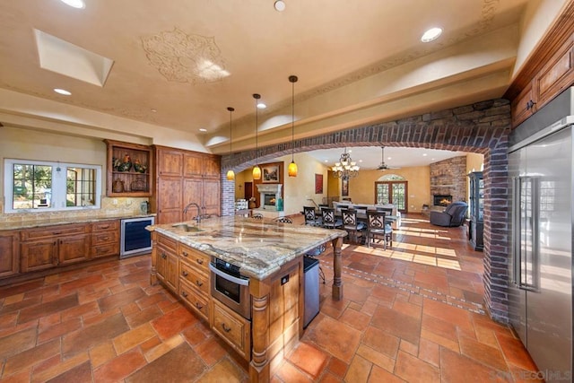 kitchen featuring decorative light fixtures, a fireplace, stainless steel appliances, and a large island with sink