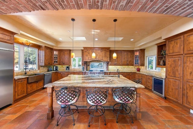 kitchen featuring a kitchen island with sink, high quality appliances, wine cooler, light stone countertops, and decorative light fixtures