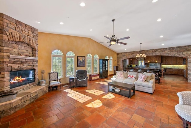 living room with lofted ceiling, a stone fireplace, and ceiling fan with notable chandelier