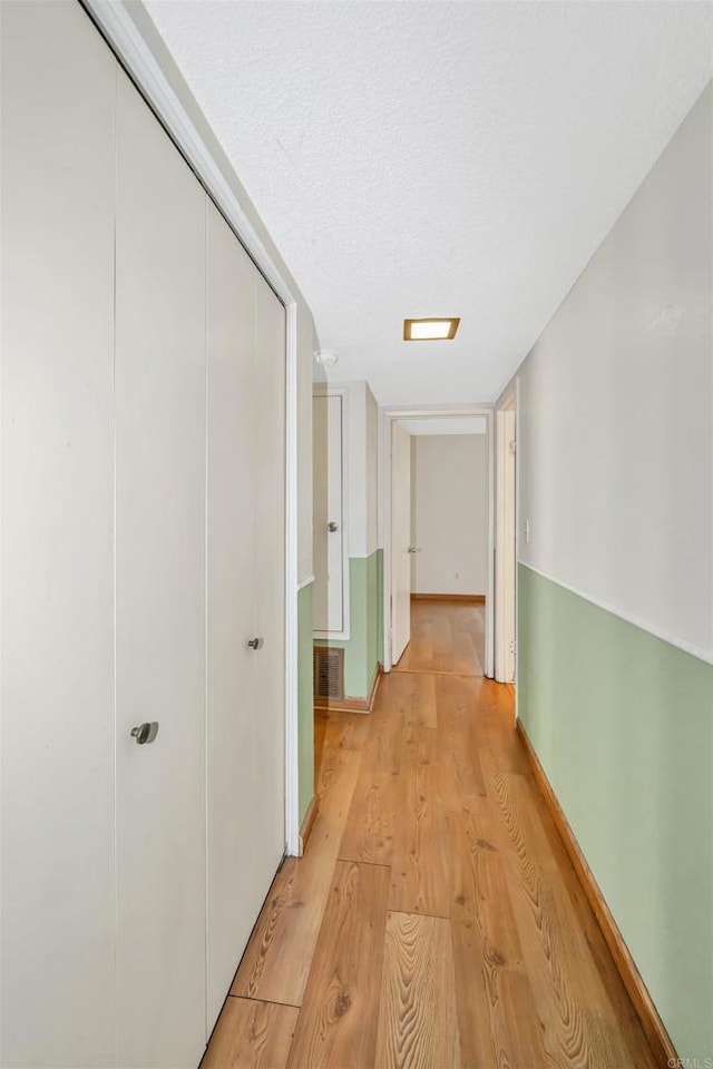 corridor with light hardwood / wood-style flooring and a textured ceiling