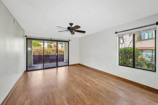 empty room featuring ceiling fan, plenty of natural light, wood-type flooring, and a textured ceiling