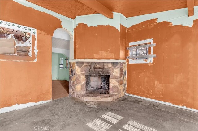 unfurnished living room featuring beamed ceiling, wood ceiling, a fireplace, and concrete floors