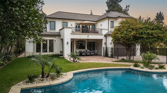 back house at dusk with a balcony, a patio area, a fenced in pool, and a yard