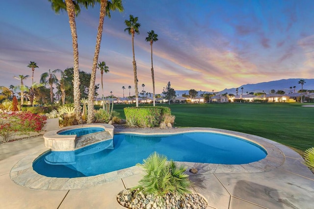 pool at dusk featuring an in ground hot tub, a patio area, and a lawn