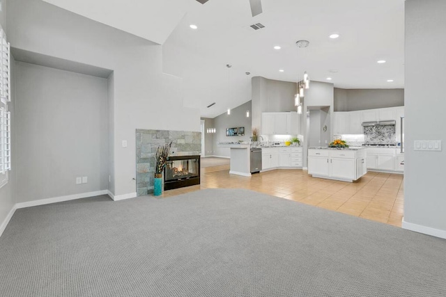 unfurnished living room featuring a multi sided fireplace, ceiling fan, light colored carpet, and high vaulted ceiling