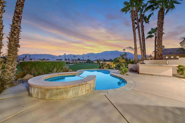 pool at dusk featuring a mountain view, a patio, and an in ground hot tub