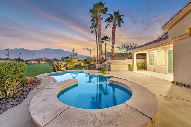 pool at dusk featuring a mountain view, an in ground hot tub, and a patio