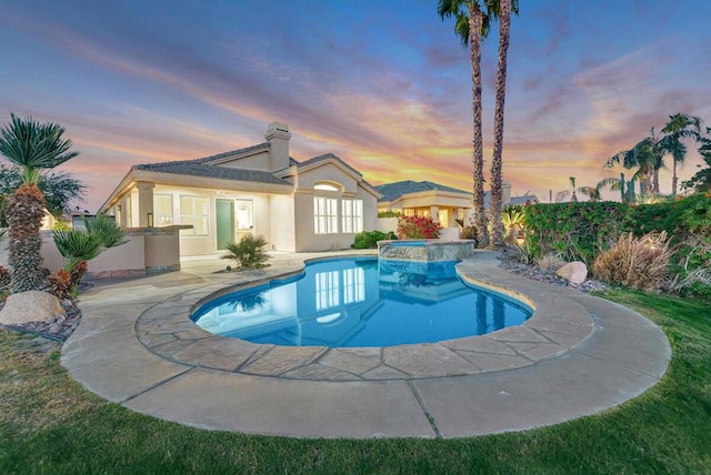 pool at dusk with an in ground hot tub and a patio