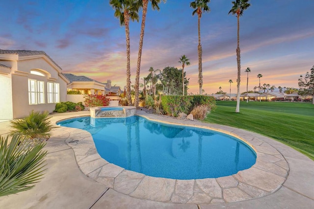 pool at dusk featuring a yard and an in ground hot tub