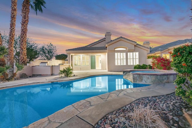 pool at dusk featuring an in ground hot tub and a patio