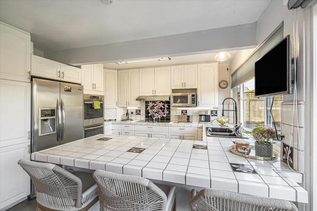 kitchen featuring sink, white cabinetry, stainless steel appliances, tile counters, and kitchen peninsula