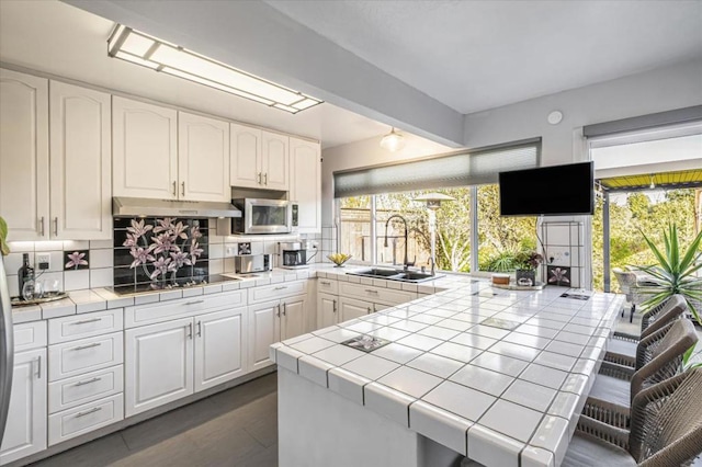 kitchen with sink, backsplash, tile counters, white cabinets, and black electric cooktop