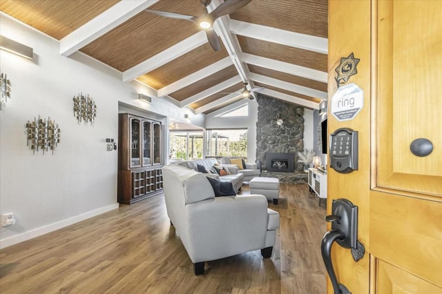 living room with ceiling fan, a stone fireplace, dark hardwood / wood-style flooring, and vaulted ceiling with beams