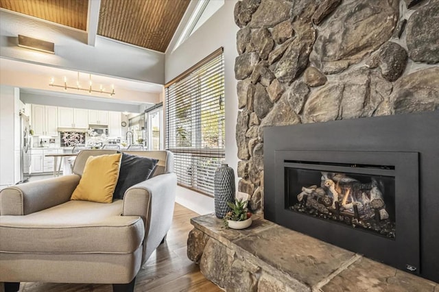 living room with hardwood / wood-style flooring, a stone fireplace, and high vaulted ceiling