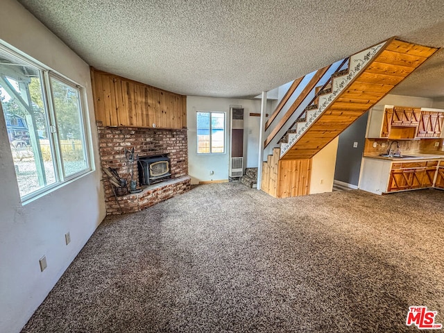 unfurnished living room featuring a textured ceiling, plenty of natural light, a wood stove, and carpet floors