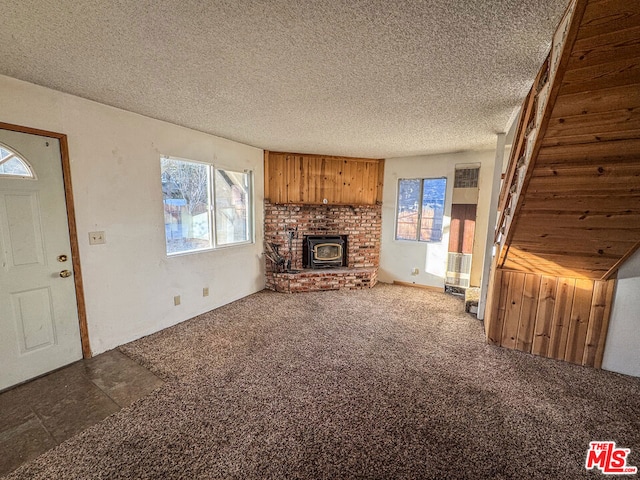 unfurnished living room with carpet flooring, a wood stove, and a textured ceiling