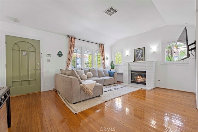 living room featuring hardwood / wood-style floors, lofted ceiling, and a brick fireplace