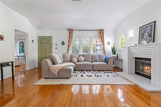 living room featuring hardwood / wood-style flooring, lofted ceiling, and a brick fireplace