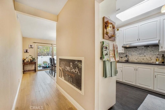 kitchen with white cabinets, dark wood-type flooring, a skylight, tasteful backsplash, and black electric cooktop