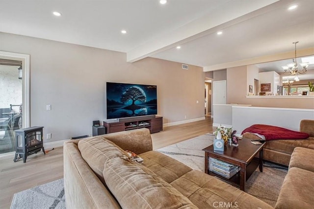 living room with a chandelier, beam ceiling, a wood stove, and light hardwood / wood-style floors