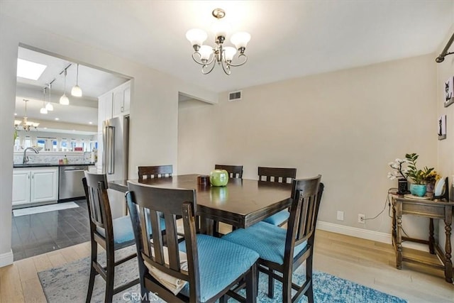 dining space with sink, light hardwood / wood-style flooring, a skylight, and a notable chandelier