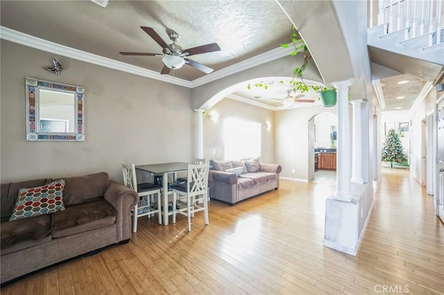 living room with crown molding, light hardwood / wood-style flooring, ceiling fan, a textured ceiling, and decorative columns