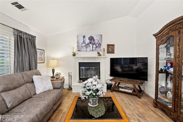 living room with a brick fireplace, light hardwood / wood-style floors, and vaulted ceiling