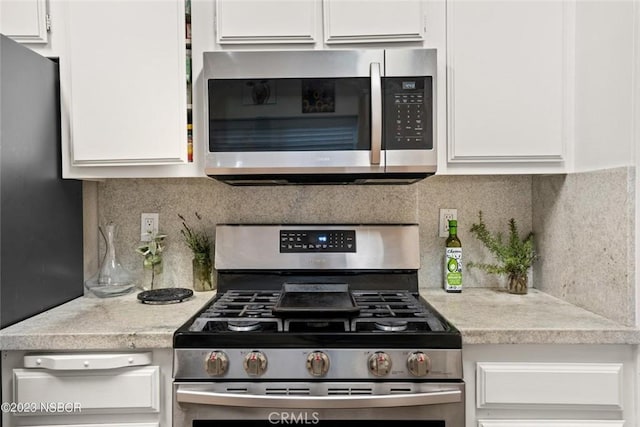 kitchen with backsplash, white cabinetry, and stainless steel appliances