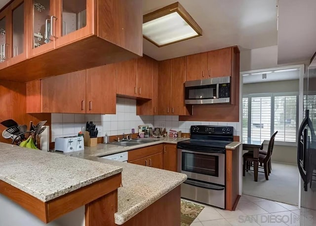 kitchen featuring kitchen peninsula, appliances with stainless steel finishes, decorative backsplash, light tile patterned flooring, and light stone countertops