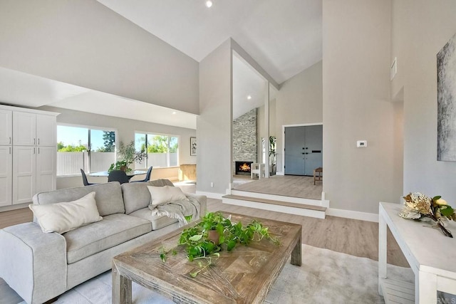 living room featuring high vaulted ceiling, light wood-type flooring, and a stone fireplace