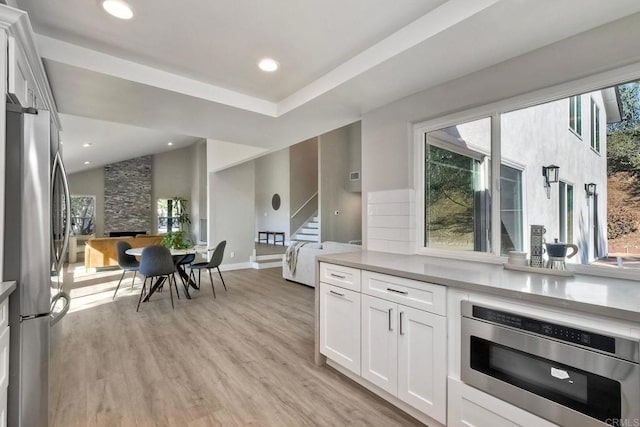 kitchen with vaulted ceiling, a fireplace, light hardwood / wood-style floors, stainless steel refrigerator, and white cabinetry