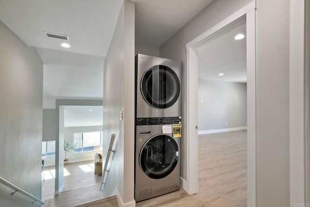 clothes washing area with light wood-type flooring and stacked washer and dryer