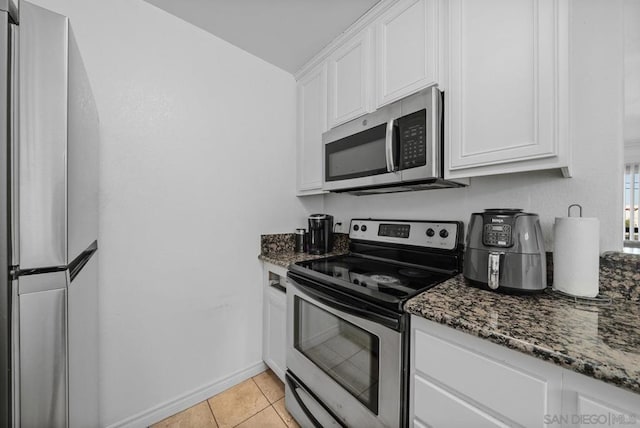 kitchen featuring light tile patterned floors, white cabinetry, stainless steel appliances, and dark stone counters