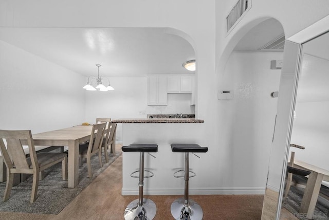 kitchen with white cabinets, hanging light fixtures, a notable chandelier, light colored carpet, and a breakfast bar area