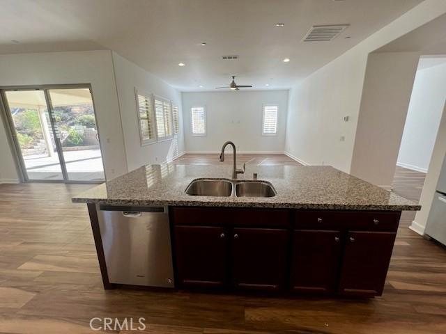 kitchen featuring dishwasher, sink, light stone counters, and dark brown cabinetry