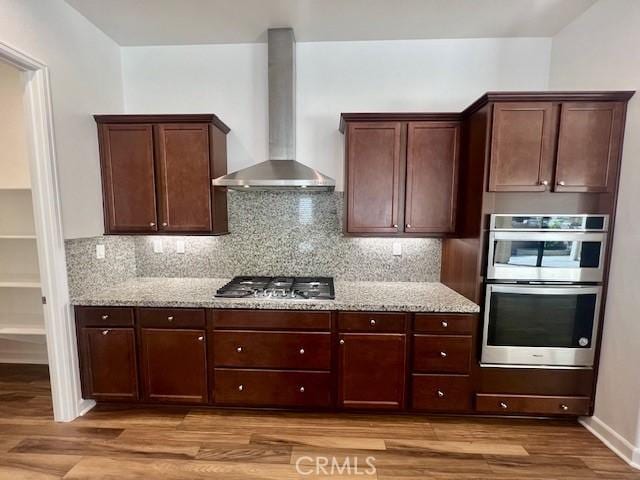 kitchen featuring light wood-type flooring, appliances with stainless steel finishes, wall chimney exhaust hood, and light stone counters