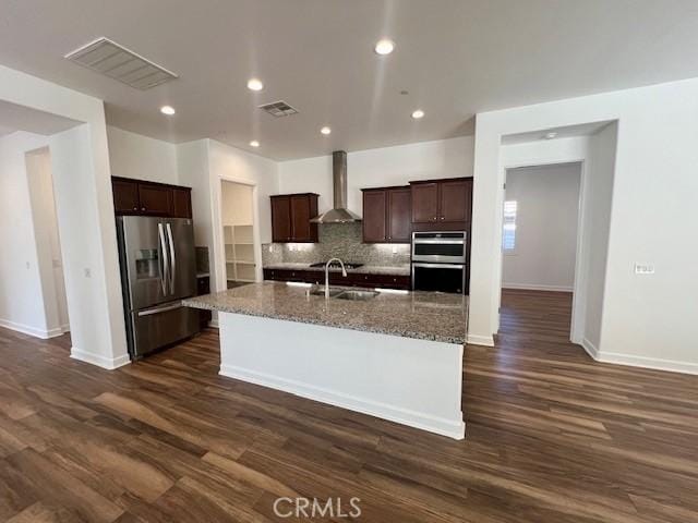 kitchen featuring an island with sink, appliances with stainless steel finishes, dark hardwood / wood-style flooring, wall chimney exhaust hood, and sink