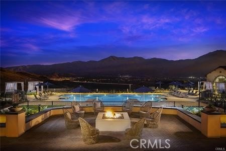 pool at dusk featuring a patio area, an outdoor fire pit, and a mountain view